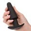 A hand model holds a black silicone anal plug for scale.