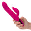 A hand model holds a pink thrusting rabbit vibrator with rolling brads for scale.