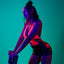 An editorial shot of a model wearing a pink UV reactive lace teddy under black light to showcase its glow-in-the dark design. 