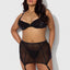 A curvy model wears a black satin bra and garter skirt with thong combining sheer mesh with smooth satin microfibre panels. 