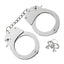 A pair of metal handcuffs lay flat on a white backdrop next to two pairs of keys.