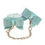 A pair of aqua iridescent bowtie ankle cuffs with diamante-studs all over it and a gold metal chain. 