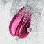 A magenta pink clitoral stimulator splashes in water showcasing its waterproof design. 