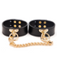 A pair of black faux leather wrist cuffs with gold hardware sits against a white backdrop. 