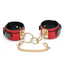 A pair of wide red faux leather wrist cuffs with gold hardware sits against a white backdrop. 