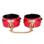 A pair of red faux leather wrist cuffs with a  T-plate bolted through the front of each cuff with gold O-rings.